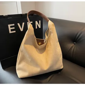 Detailed view of a beige suede hobo shoulder bag with brown handle on dark leather couch.