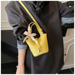 Detailansicht einer leuchtend gelben Eimer Tasche mit Muster, Schal und elegantem Schloss.