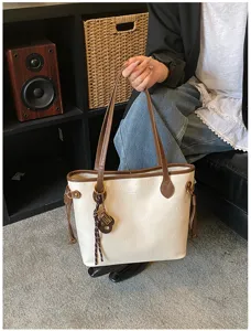 Detailed shot of stylish minimalist two-tone tote bag with brown straps and cute charm accent.