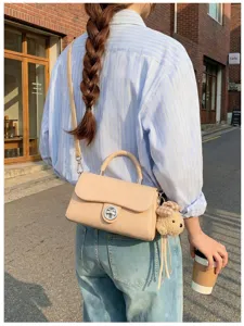 Vista dettagliata di una borsa a tracolla beige chic con chiusura a torsione e ciondolo.