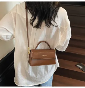 Close-up view of the chic brown top-handle crossbody bag worn on the back against stairs.