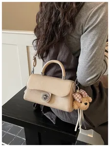 Dettaglio di una elegante borsa a tracolla beige strutturata con chiusura e ciondolo.