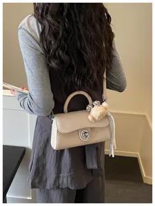 Bellissimo dettaglio di borsa a tracolla beige chic con chiusura metallica e orsetto.
