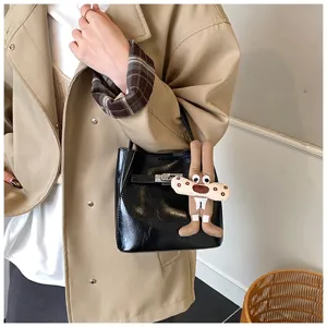 Dettaglio di una borsa a secchiello in pelle verniciata nera con ciondolo peluche e chiusura.