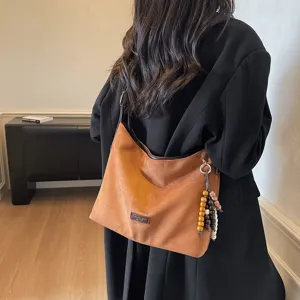 Detail view of a brown suede shoulder bag featuring a stylish beaded charm and retro commuter style.