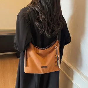 Retro brown suede underarm shoulder bag detail showing textured fabric and beaded pendant accessory.