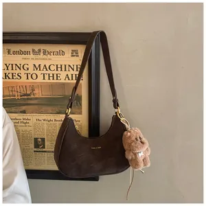 Detailed view of brown suede shoulder bag featuring fluffy bear keychain and vintage setting.