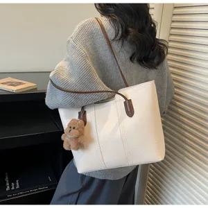 Vista dettagliata di una elegante borsa tote bianca con manici marroni e ciondolo orsetto.