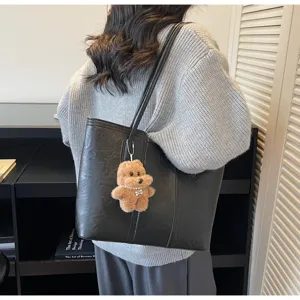 Vista dettagliata di una borsa tote in pelle nera con un simpatico ciondolo orsetto.