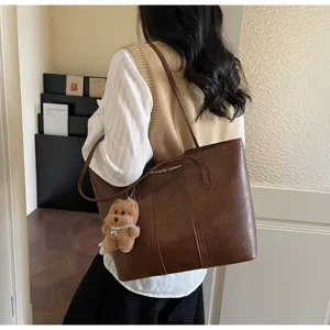 Vista dettagliata di una borsa shopper marrone in pelle PU con ciondolo orsetto peluche.