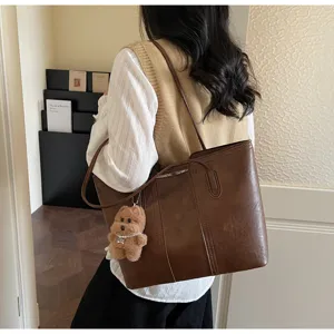 Dettaglio borsa tote in pelle marrone retrò, borsa a tracolla casual con grazioso ciondolo orsetto.