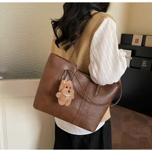 Vista dettagliata di una elegante borsa tote in pelle PU marrone con ciondolo orsetto.