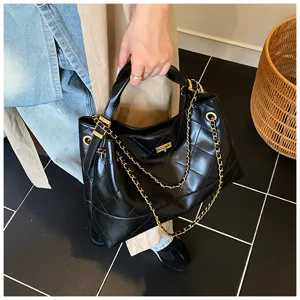 Detalle de bolso de mano de cuero acolchado negro con correa de cadena dorada y cierre de giro.