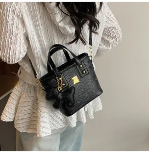 Detailed shot of black textured bucket bag with top handles, gold hardware, and cute bear charm.