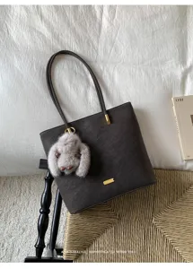 Detailansicht der dunkelgrauen Tasche mit niedlichem Plueschanhaenger und eleganter Metallplatte.