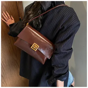 Dettaglio borsa a spalla in pelle cerata marrone scuro, stile elegante con chiusura geometrica.