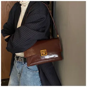 Borsa a spalla marrone scuro in pelle cerata con elegante chiusura metallica raffinata.