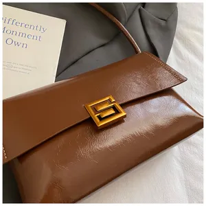 Borsa a spalla marrone in pelle cerata con elegante chiusura geometrica in metallo.