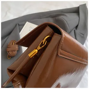 Vista dettagliata della borsa a spalla marrone in pelle verniciata morbida con accessori.