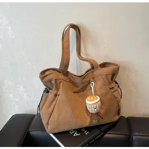 Vista dettagliata di una borsa tote in velluto a coste marrone con ciondolo in peluche.