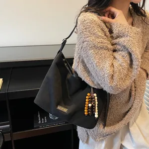 Black casual shoulder bag detail view featuring metal tag and wooden bead tassel charm.
