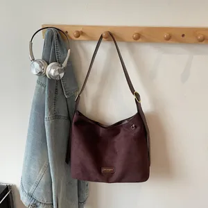 Detailed view of retro suede hobo shoulder bag hanging on wooden wall hook in room.