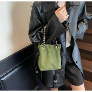 Green suede chain drawstring bucket bag detail showcasing texture, metal hardware and strap.