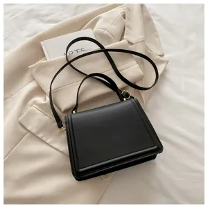 Sac bandoulière noir minimaliste en cuir avec des détails métalliques dorés chic.