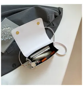 Sac bandoulière blanc minimaliste avec chaîne et rabat, ouvert avec des articles du quotidien.