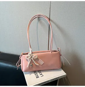 Pink shoulder bag detail view featuring delicate pearl bow pendant, lace trim and long thin straps.