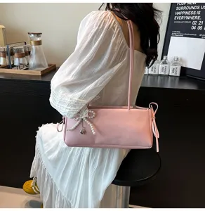 Detailed view of the elegant pink shoulder bag with pearl bow pendant in stylish scene setting.