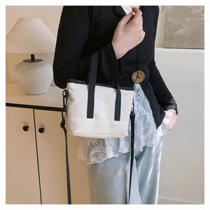 Minimalist canvas crossbody bag for women, small casual shoulder handbag with black handles.
