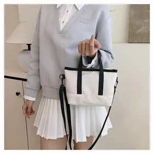 Detailed view of a chic white canvas tote bag with black contrast trim and shoulder strap.