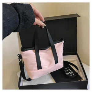 Pink canvas crossbody bag detail view, featuring black handles and adjustable strap design.