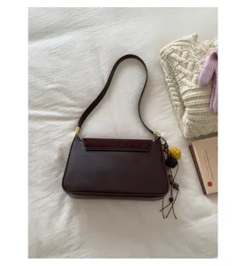 Detailaufnahme der braunen Schultertasche mit Wildlederlasche, Lederkorpus und schickem Anhänger.