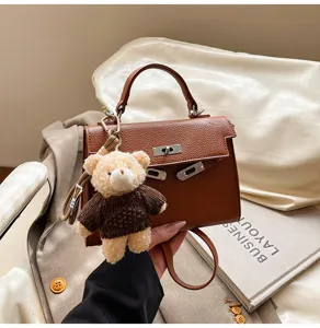 Detalle de bolso de mano Kelly de cuero marron retro con un lindo colgante de oso de peluche.