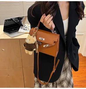 Detalle de bolso de cuero marrón retro con lindo dije de osito de peluche y elegante cierre de metal.