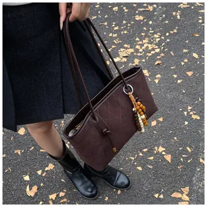 Dettaglio borsa tote trapuntata in camoscio marrone con pendente in perline di legno e doppi manici.