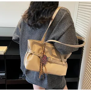 Vista di dettaglio dell'elegante borsa a spalla in vernice beige con cintura chic e ciondolo.