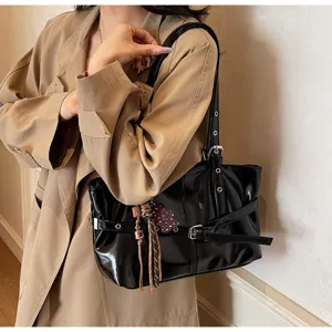 Dettaglio borsa a spalla in pelle verniciata nera, fibbia elegante, stile quotidiano.