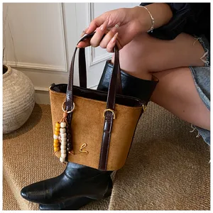 Brown suede bucket bag detail shot showing metallic logo and decorative bead charm.