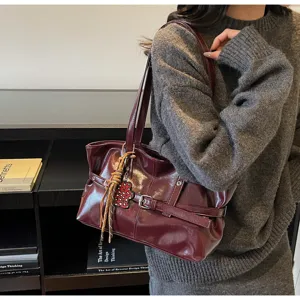 Vista dettagliata della borsa tote elegante in pelle verniciata bordeaux con fibbia e ciondolo.