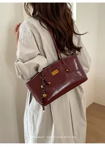 Detalle del bolso de hombro de cuero burdeos con diseño vintage y placa de metal dorada.