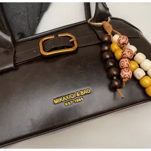 Brown leather underarm bag detail showing retro metal buckle and decorative wooden bead pendant.