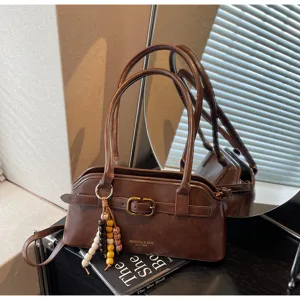 Close-up of brown vintage leather shoulder bag with buckle and beaded charm detail.