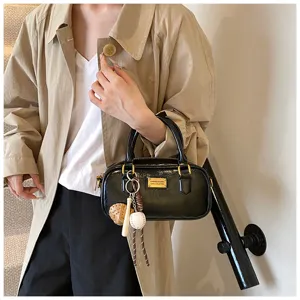 Stylish black patent leather boston handbag with baseball charm, perfect for daily commute.