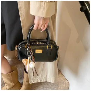 Detail view of the black patent leather Boston bag with chic baseball keychain and gold hardware.