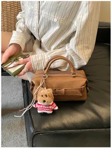 Detailed shot of a stylish brown leather bowling Boston bag with cute bear keychain charm.