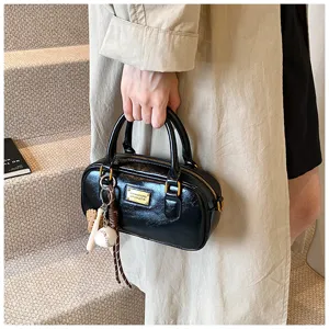 Close-up detail of black leather Boston handbag with gold hardware and baseball keychain charm.
