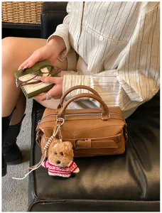 Detail shot of the brown leather Boston bag featuring chic strap buckle and cute bear pendant.